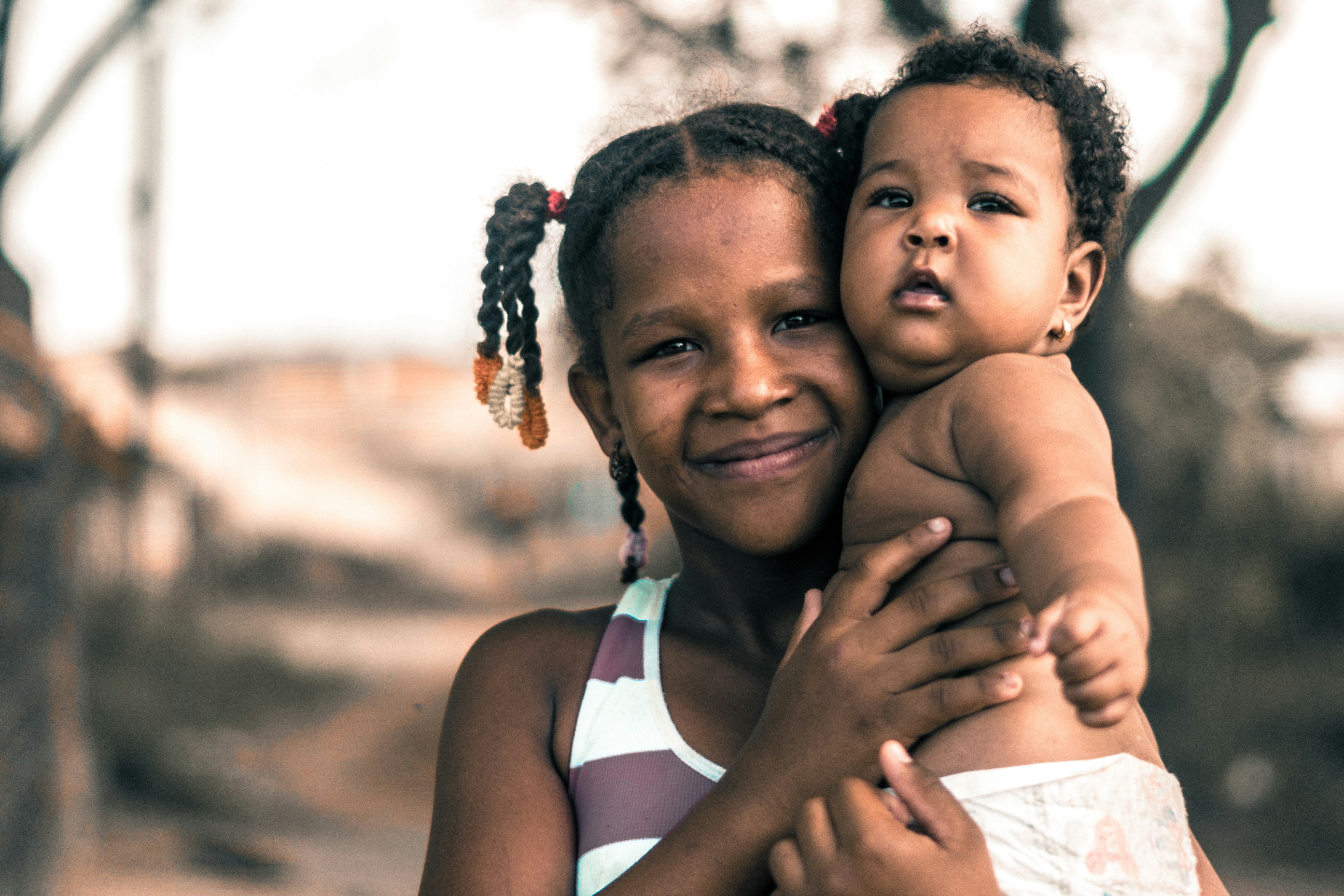 A young girl holding her baby sibling, both looking warmly at the camera