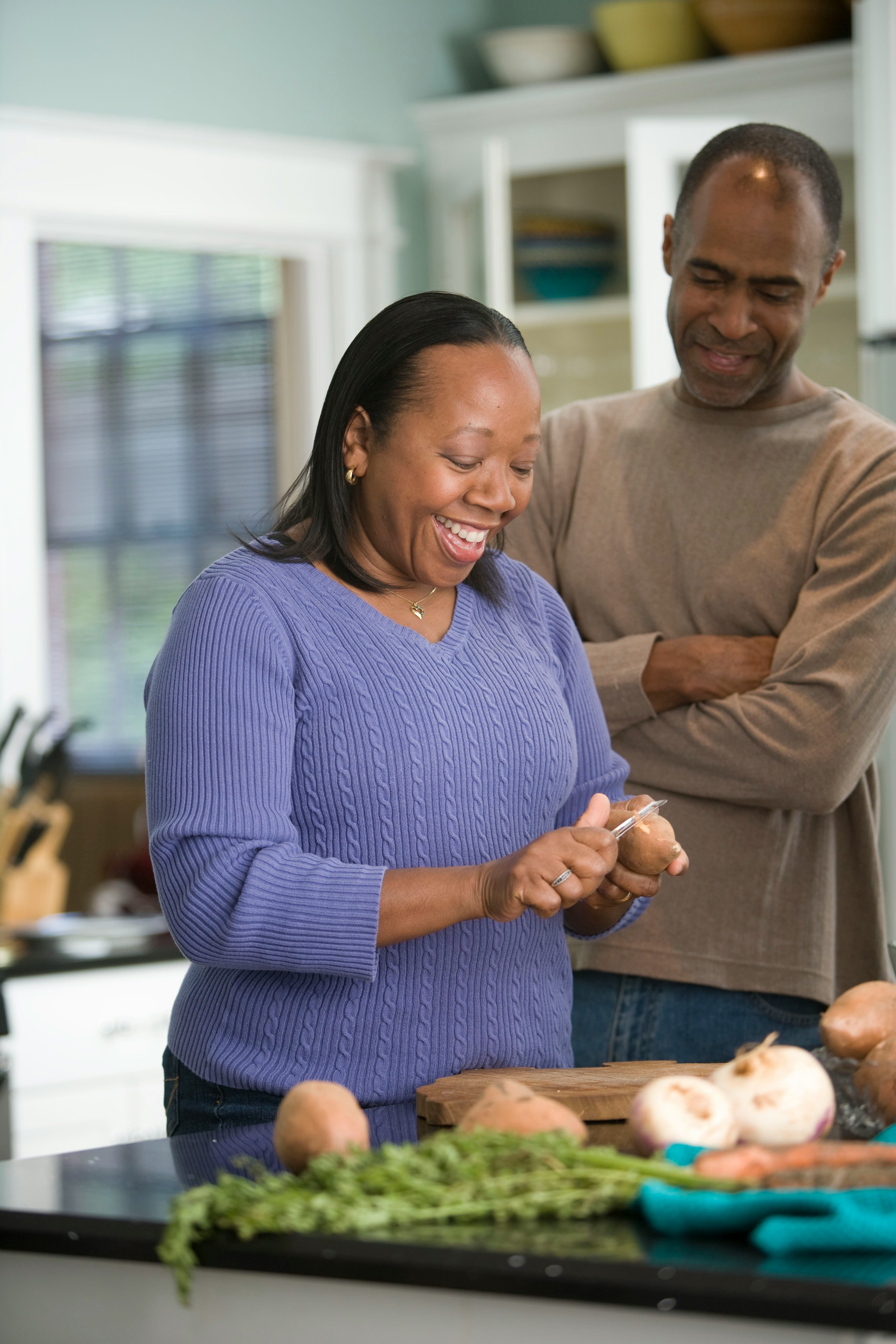 A couple relaxed at home in their kitchen, preparing food together and smiling